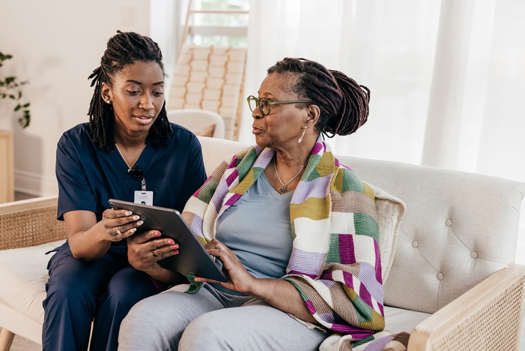 nurse sitting on couch with older woman looking at tablet