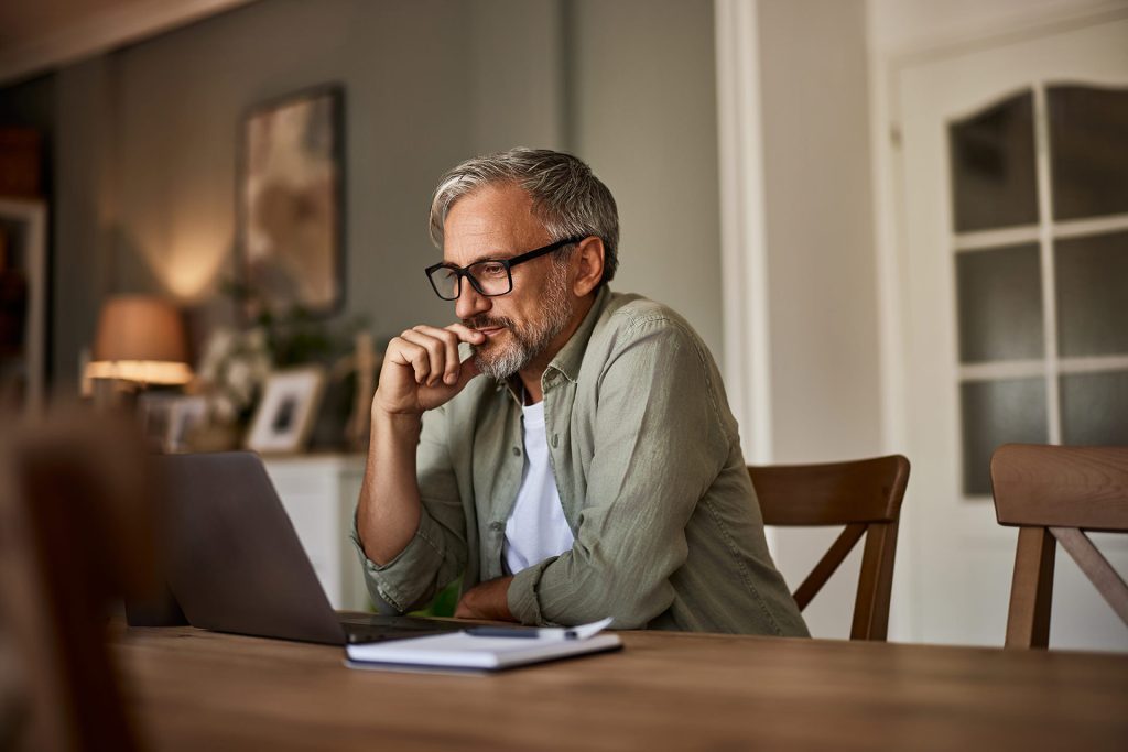 A senior male reading an online document on a laptop.